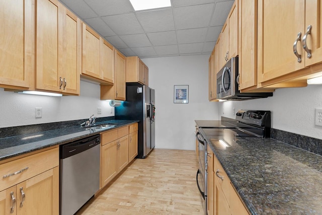 kitchen with sink, dark stone counters, stainless steel appliances, light brown cabinets, and light hardwood / wood-style flooring