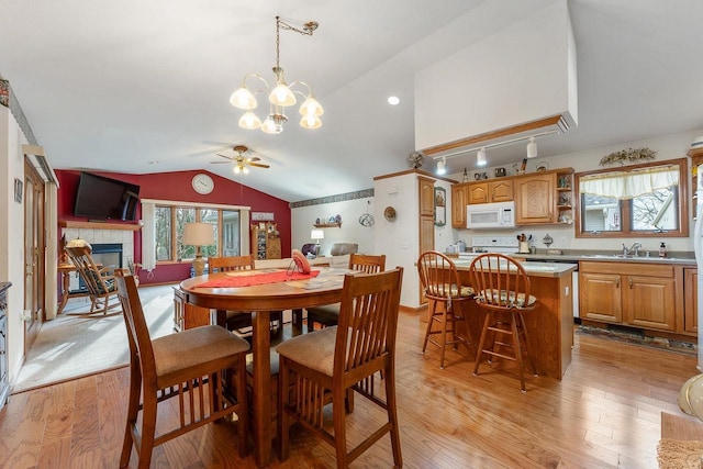 dining area featuring ceiling fan with notable chandelier, a fireplace, sink, vaulted ceiling, and light hardwood / wood-style flooring