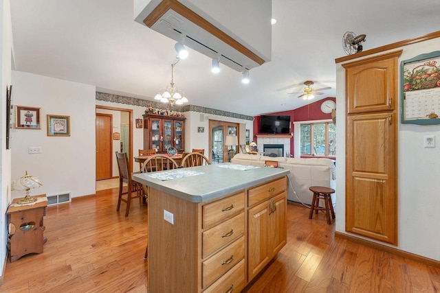 kitchen with hanging light fixtures, a kitchen island, light hardwood / wood-style flooring, ceiling fan with notable chandelier, and lofted ceiling