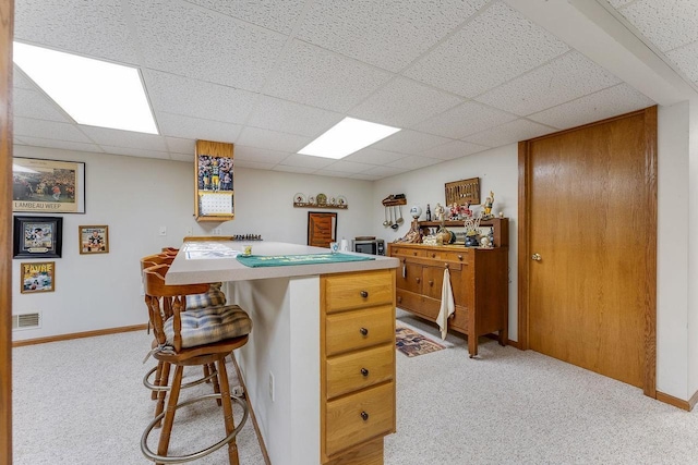 kitchen featuring light carpet, a paneled ceiling, a center island, and a breakfast bar area