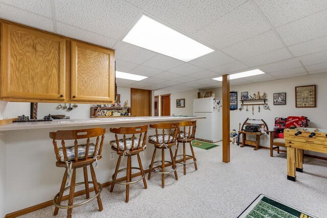 kitchen featuring light carpet, white refrigerator, a kitchen bar, and kitchen peninsula