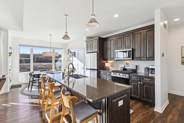 kitchen featuring a breakfast bar area, dark brown cabinets, a center island with sink, pendant lighting, and stainless steel appliances