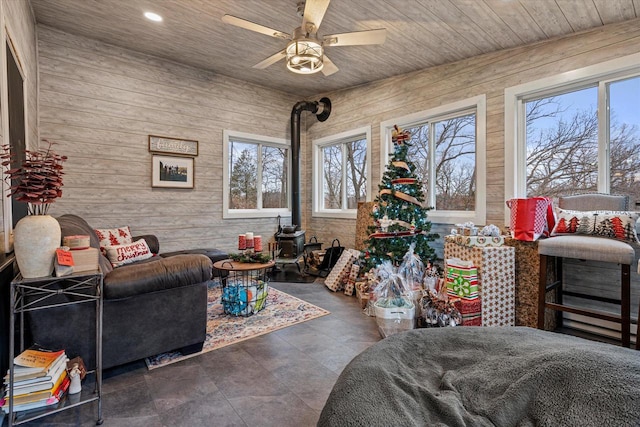 living room featuring ceiling fan, a wood stove, wooden walls, and wood ceiling