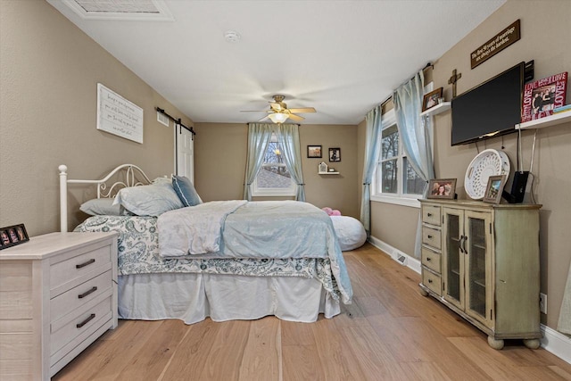 bedroom featuring a barn door, ceiling fan, and light wood-type flooring