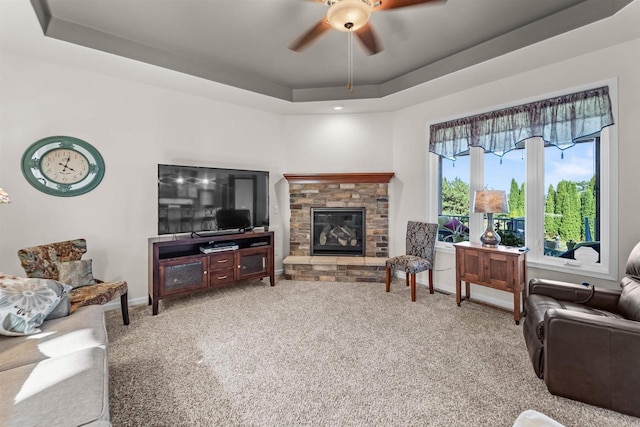 living room featuring carpet, a stone fireplace, ceiling fan, and a tray ceiling