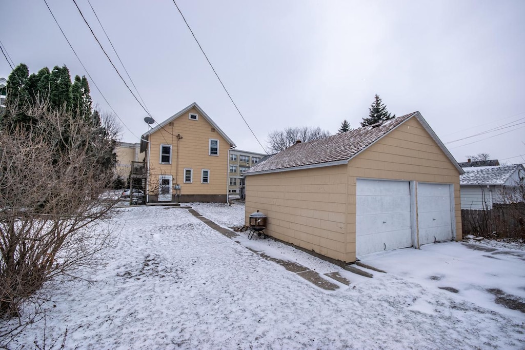 snow covered house featuring a garage and an outbuilding