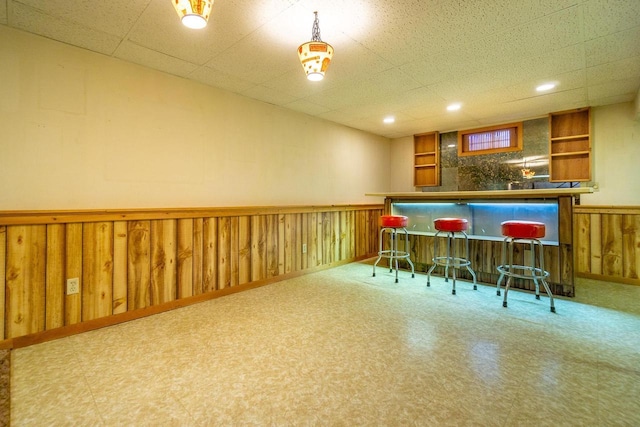 bar featuring pendant lighting, a paneled ceiling, and wood walls