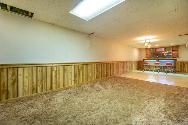 basement featuring indoor bar, wooden walls, a paneled ceiling, and carpet