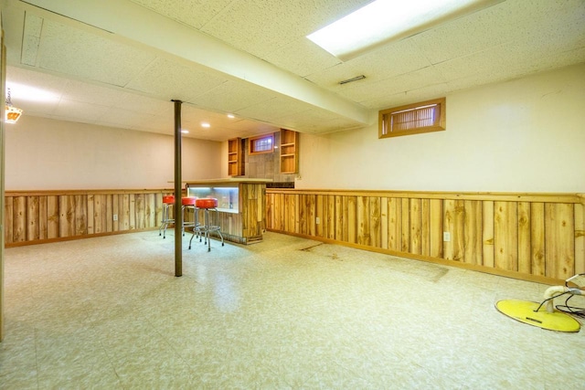 basement with indoor bar, a paneled ceiling, and wood walls