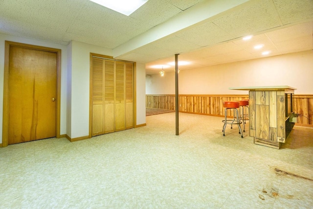 basement featuring a drop ceiling, bar area, and wooden walls