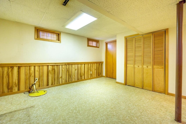 basement with a drop ceiling and wooden walls