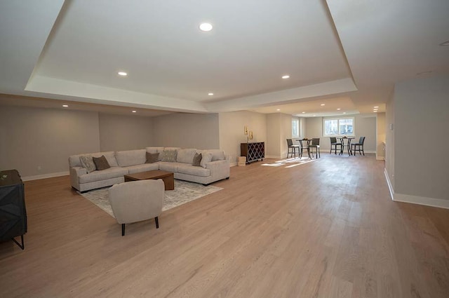 living room with a tray ceiling and light wood-type flooring