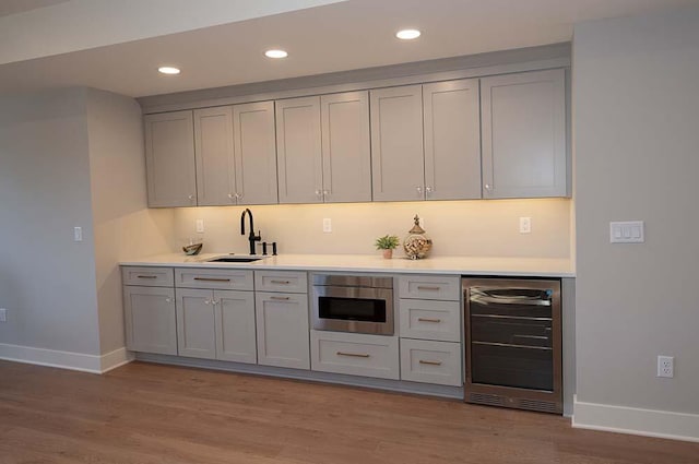 bar featuring wine cooler, sink, gray cabinetry, and light wood-type flooring