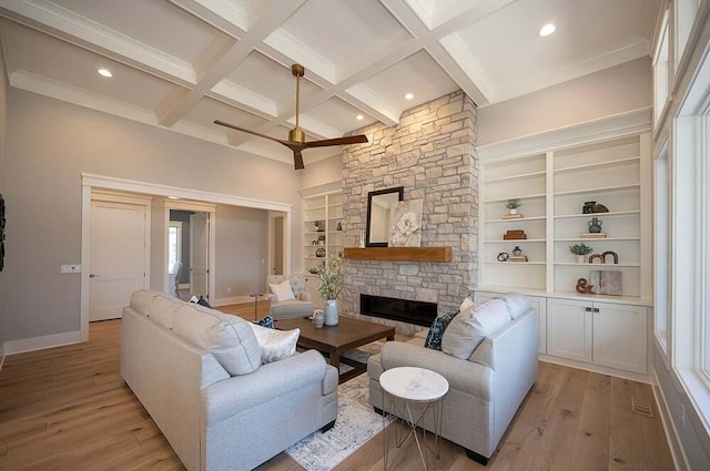 living room featuring a stone fireplace, built in features, light wood-type flooring, coffered ceiling, and beam ceiling