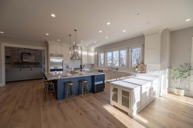 kitchen featuring a spacious island, white cabinetry, built in refrigerator, decorative light fixtures, and light stone countertops