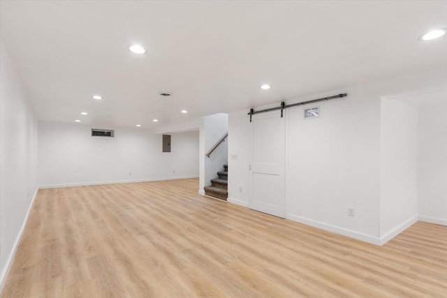 basement featuring a barn door, electric panel, and light wood-type flooring