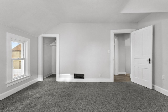 unfurnished bedroom with lofted ceiling, a closet, and dark colored carpet