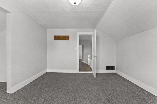 additional living space with dark colored carpet, vaulted ceiling, and a textured ceiling