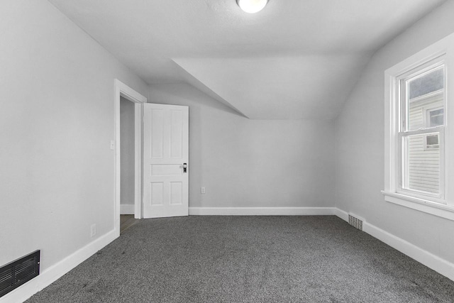 additional living space with dark colored carpet, vaulted ceiling, and a wealth of natural light