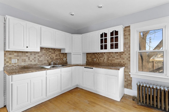 kitchen featuring radiator, sink, white cabinets, backsplash, and light hardwood / wood-style flooring