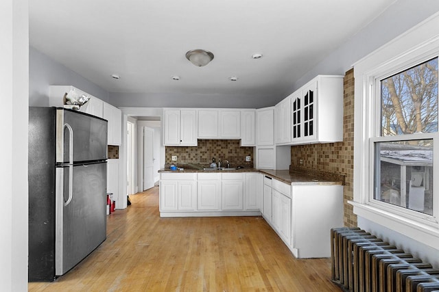 kitchen featuring decorative backsplash, radiator heating unit, stainless steel fridge, and white cabinets