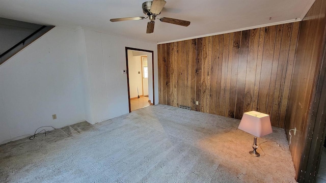 unfurnished room featuring crown molding, light carpet, ceiling fan, and wooden walls