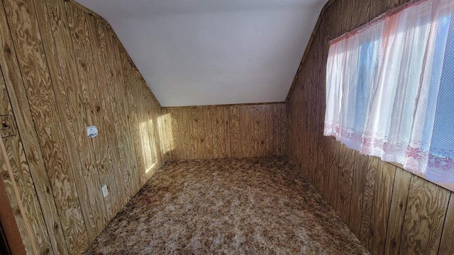 bonus room featuring lofted ceiling, carpet, and wood walls