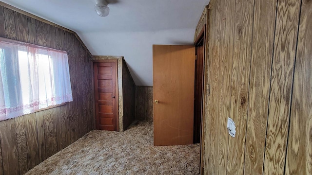 hallway with lofted ceiling, dark carpet, and wooden walls