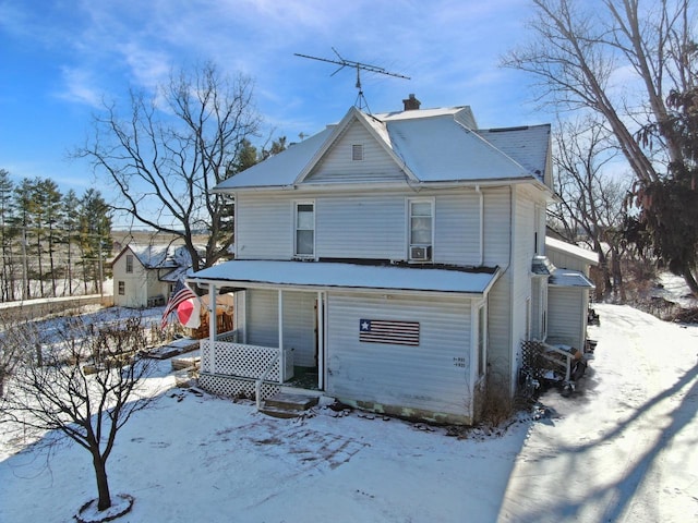 snow covered rear of property featuring covered porch