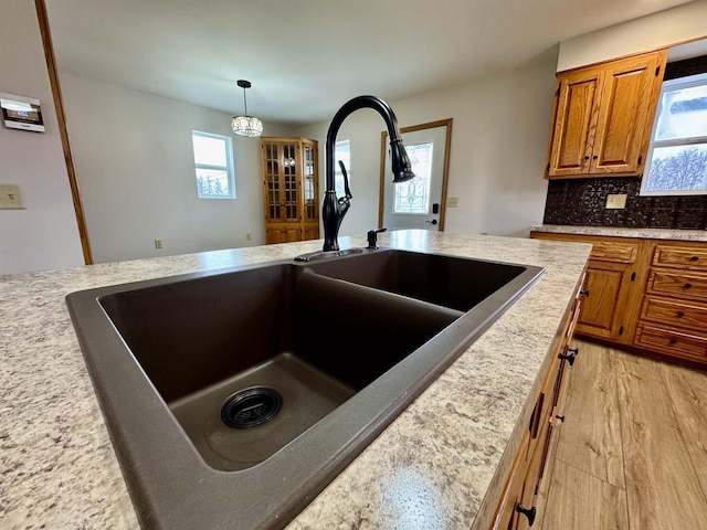 kitchen featuring sink, hanging light fixtures, light wood-type flooring, plenty of natural light, and backsplash