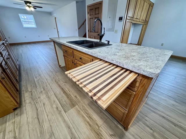 kitchen with ceiling fan, an island with sink, sink, and light wood-type flooring