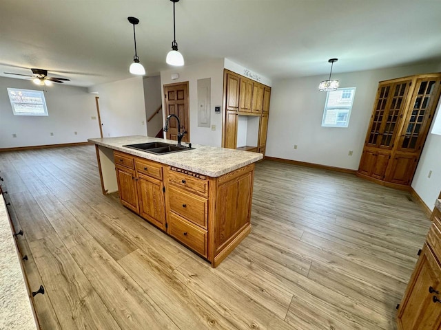 kitchen with decorative light fixtures, sink, a kitchen island with sink, ceiling fan, and light hardwood / wood-style flooring