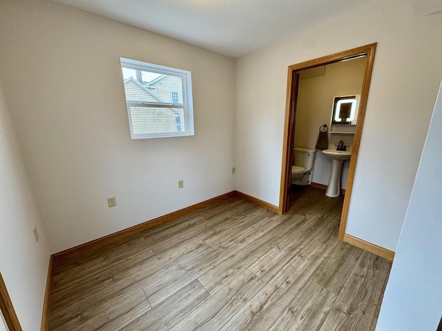 unfurnished bedroom with sink, ensuite bath, and light wood-type flooring