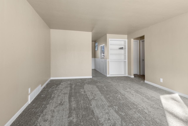 unfurnished room featuring dark colored carpet and built in shelves