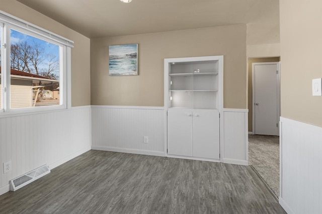 unfurnished room featuring built in shelves and dark hardwood / wood-style floors