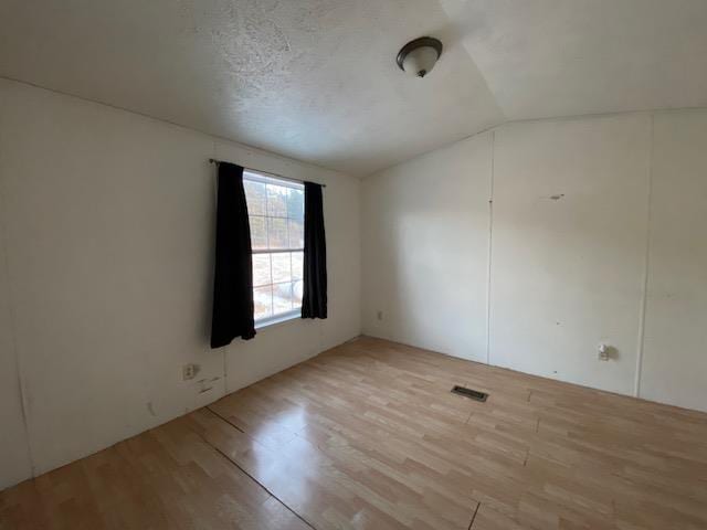 unfurnished room featuring lofted ceiling, light hardwood / wood-style floors, and a textured ceiling