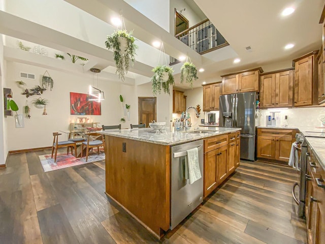 kitchen with sink, hanging light fixtures, stainless steel appliances, dark hardwood / wood-style floors, and an island with sink