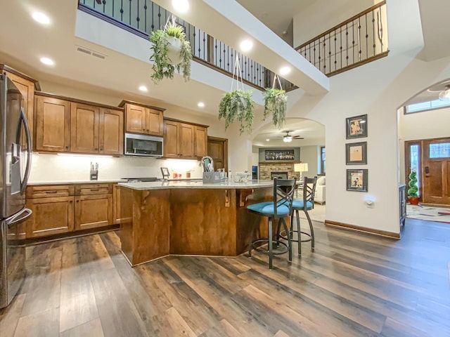 kitchen with appliances with stainless steel finishes, dark hardwood / wood-style floors, a breakfast bar, a towering ceiling, and an island with sink