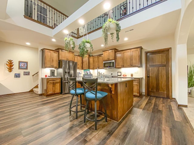 kitchen featuring a high ceiling, appliances with stainless steel finishes, dark wood-type flooring, and a kitchen breakfast bar