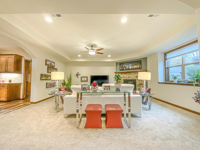 carpeted dining space featuring a tray ceiling, a fireplace, and ceiling fan