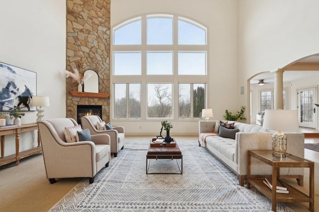 living room with a towering ceiling, a fireplace, decorative columns, light colored carpet, and ceiling fan