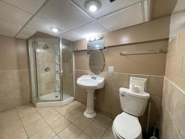 bathroom featuring tile patterned floors, toilet, a shower with shower door, and tile walls