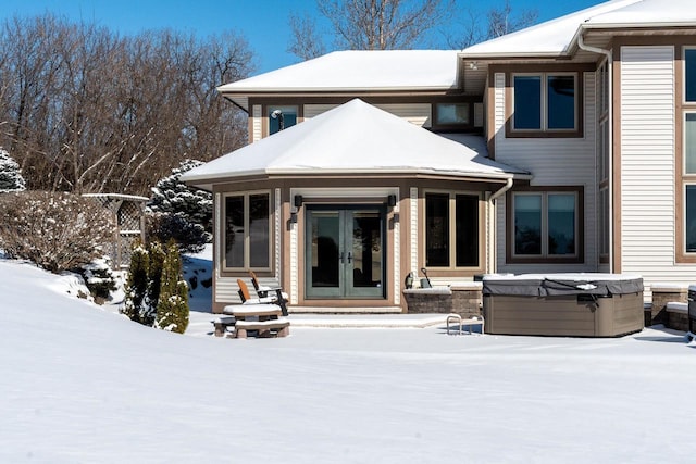 snow covered rear of property with french doors and a hot tub