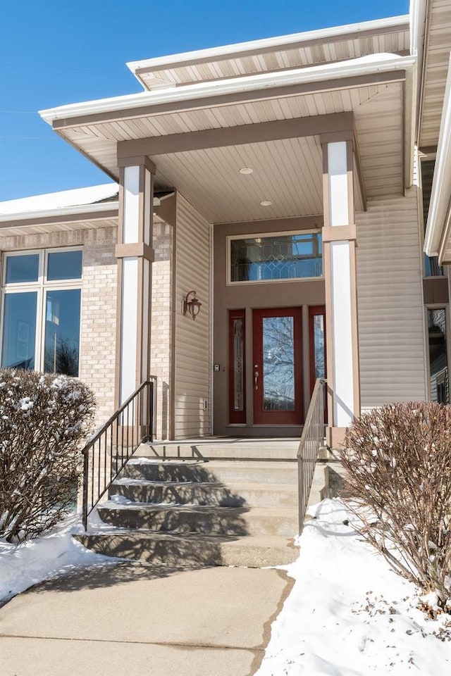 snow covered property entrance featuring brick siding