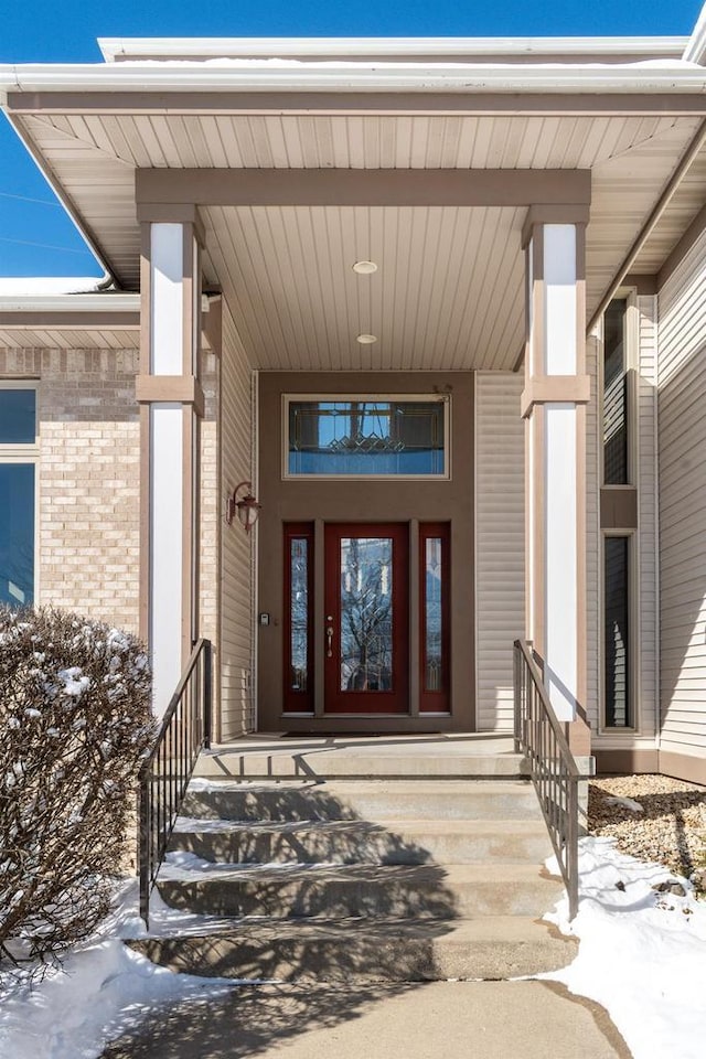 snow covered property entrance featuring a porch and brick siding