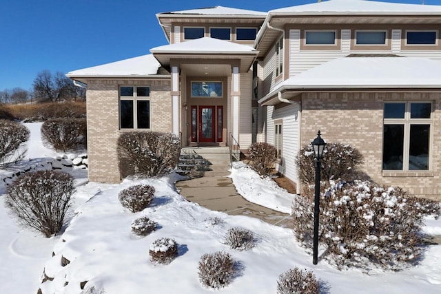 snow covered property entrance featuring brick siding