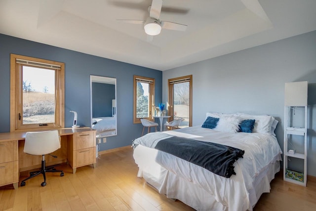 bedroom featuring light wood finished floors, a tray ceiling, a ceiling fan, and baseboards