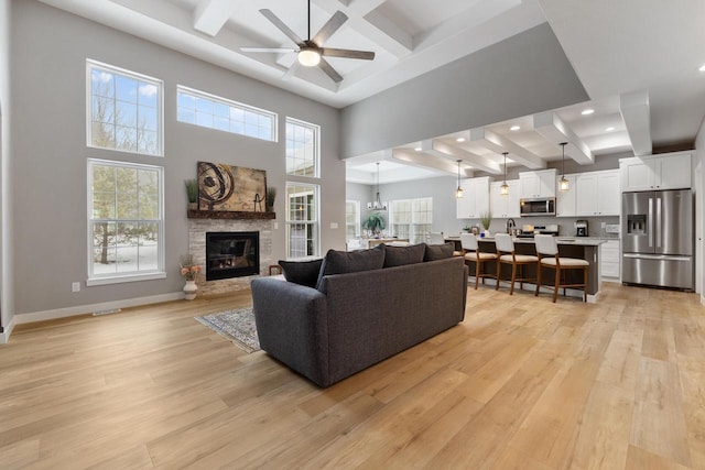 living room with coffered ceiling, a stone fireplace, beamed ceiling, and light wood-type flooring