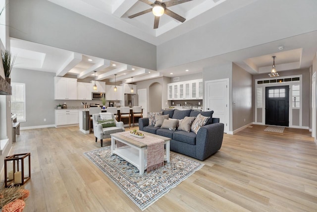 living room with a high ceiling, ceiling fan, light wood-type flooring, and a tray ceiling