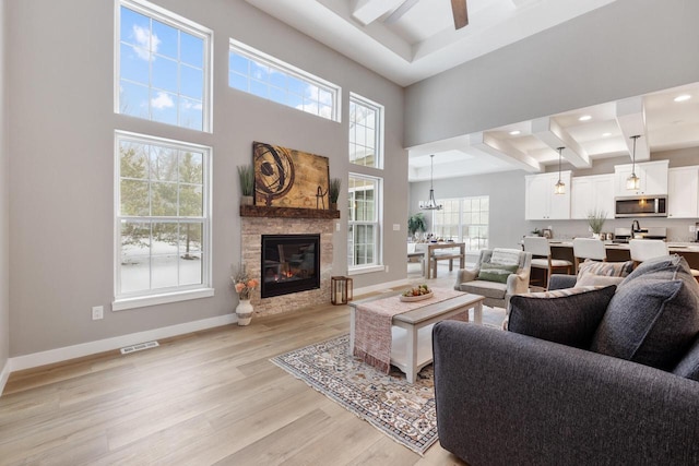 living room with a towering ceiling, a fireplace, light hardwood / wood-style floors, and ceiling fan with notable chandelier